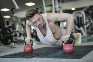 Low angle of powerful male bodybuilder in sportswear pushing up on kettlebells during training and looking at camera